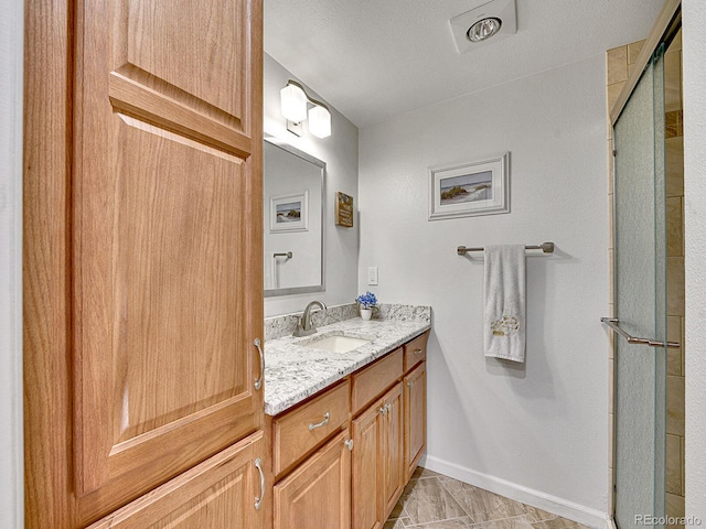 full bathroom featuring baseboards, a shower with shower door, and vanity