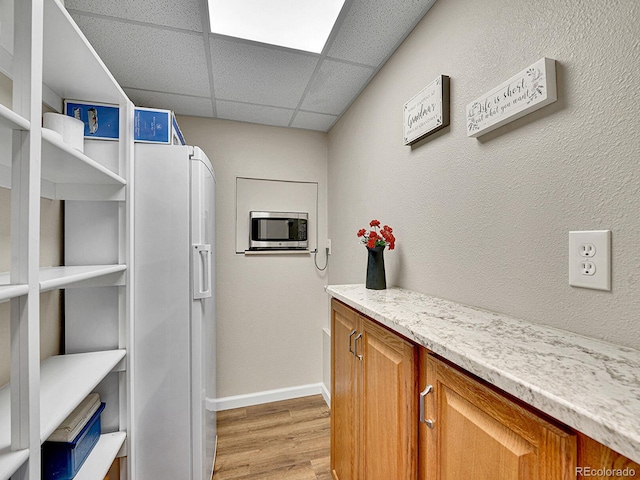 interior space with light wood-style floors, baseboards, a drop ceiling, stainless steel microwave, and brown cabinets