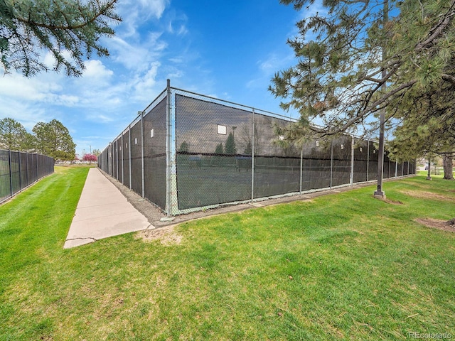 view of tennis court with a lawn and fence