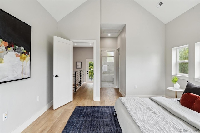 bedroom with ensuite bath, high vaulted ceiling, multiple windows, and light wood-type flooring