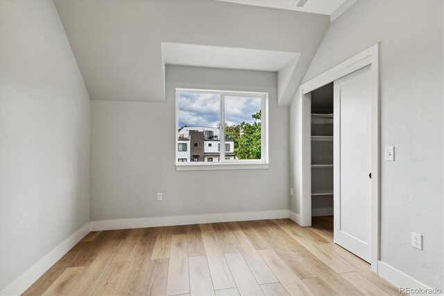 unfurnished bedroom with lofted ceiling, a closet, and light wood-type flooring