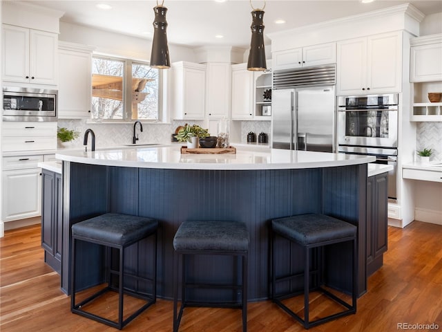 kitchen with tasteful backsplash, built in appliances, white cabinets, and a large island