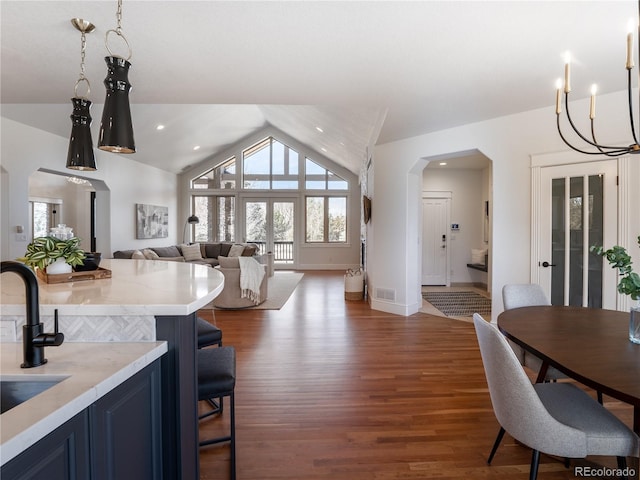 kitchen with blue cabinetry, a kitchen breakfast bar, lofted ceiling, light stone countertops, and dark hardwood / wood-style floors