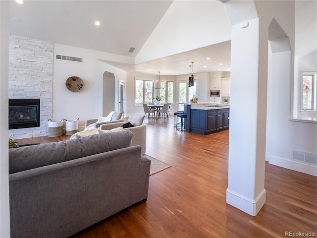 living room featuring high vaulted ceiling, a stone fireplace, a chandelier, and light hardwood / wood-style floors