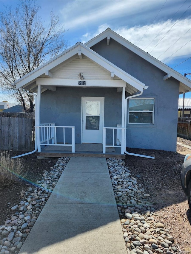 view of front of home with fence, a porch, and stucco siding