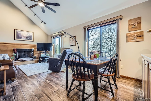 dining space with a fireplace with raised hearth, wood finished floors, a ceiling fan, and track lighting