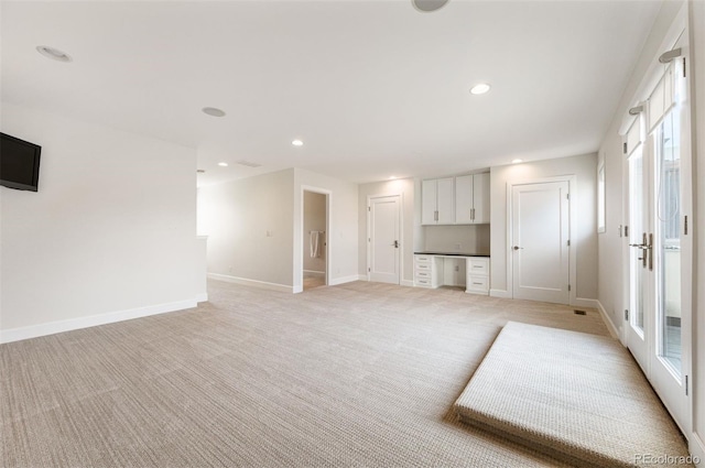 unfurnished living room with built in desk and light colored carpet