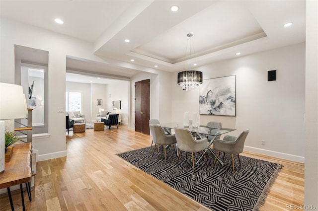 dining area featuring an inviting chandelier, light wood-type flooring, and a tray ceiling