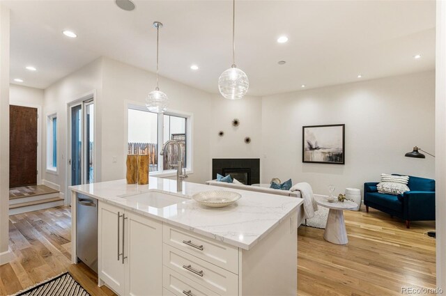 kitchen with sink, hanging light fixtures, light stone countertops, white cabinets, and stainless steel dishwasher