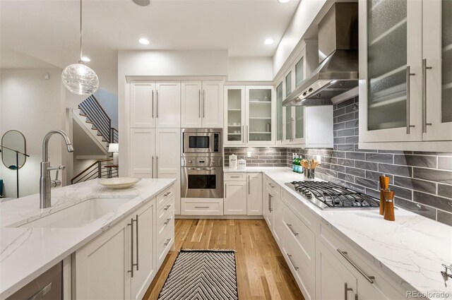 kitchen with sink, decorative light fixtures, appliances with stainless steel finishes, light stone countertops, and wall chimney range hood