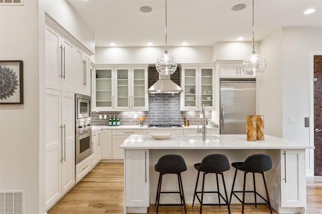 kitchen featuring sink, a kitchen island with sink, built in appliances, and white cabinets