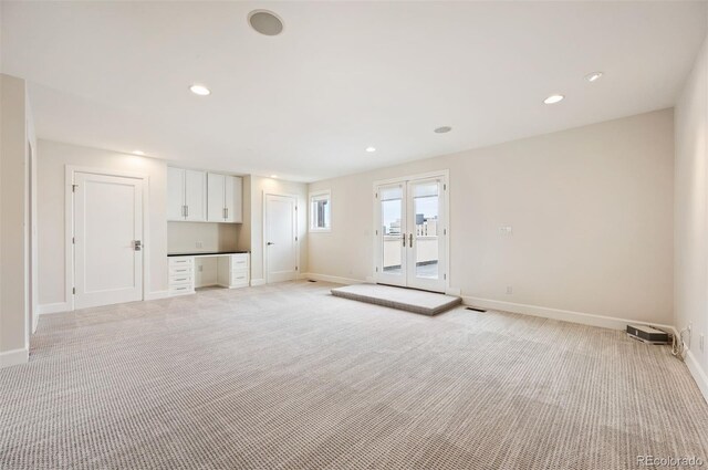 unfurnished living room with light carpet, built in desk, and french doors