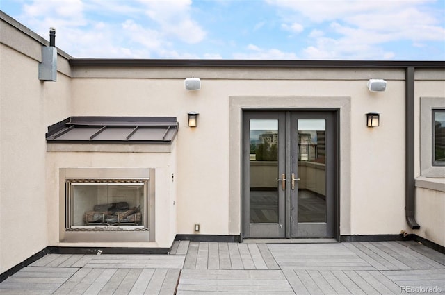 property entrance featuring a wooden deck, exterior fireplace, and french doors