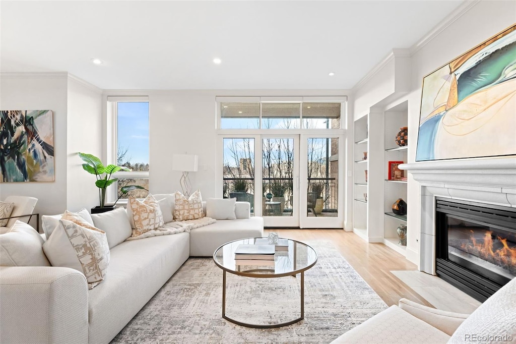 living room with built in shelves, ornamental molding, and light hardwood / wood-style floors