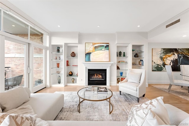 living room featuring crown molding, built in features, and light hardwood / wood-style flooring