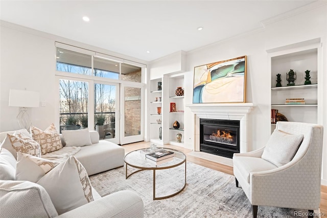 living room featuring built in shelves, ornamental molding, and light wood-type flooring