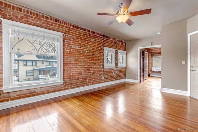 empty room with light hardwood / wood-style floors, ceiling fan, and brick wall