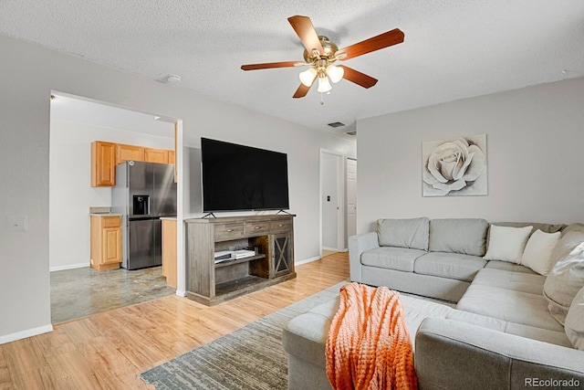 living room featuring ceiling fan, a textured ceiling, and light hardwood / wood-style flooring