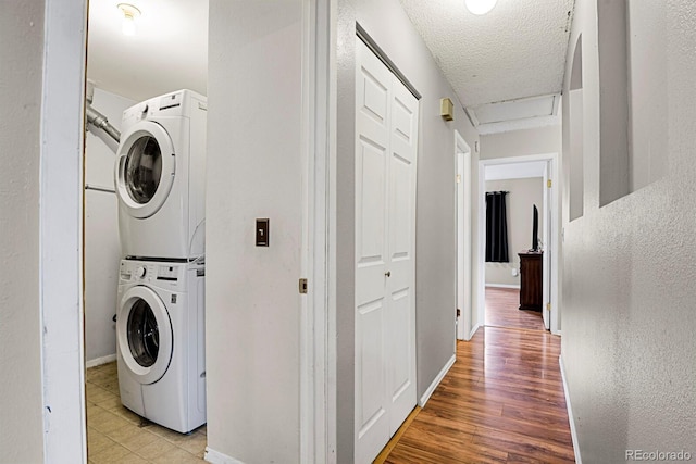 clothes washing area featuring stacked washer / drying machine, light wood-type flooring, and a textured ceiling