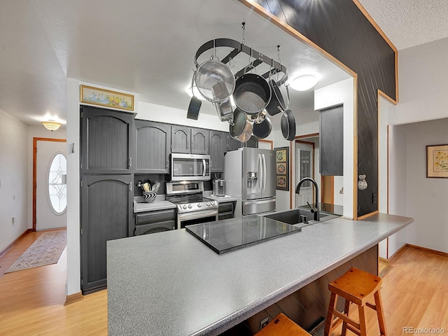 kitchen featuring stainless steel appliances, gray cabinetry, a sink, and light wood finished floors