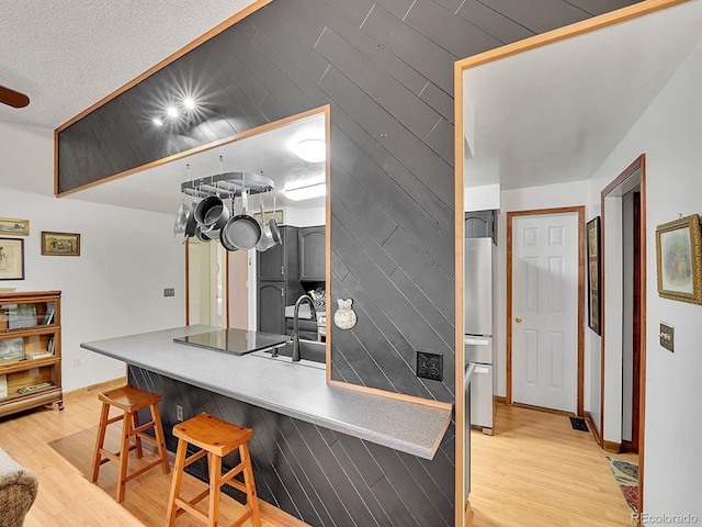 kitchen with light wood finished floors, baseboards, a breakfast bar area, a textured ceiling, and fridge