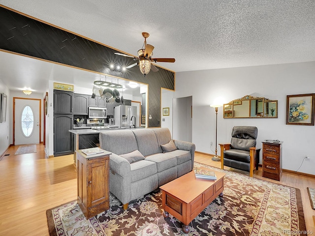 living area featuring light wood-style floors, vaulted ceiling, a textured ceiling, and a ceiling fan