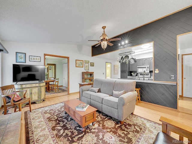 living room featuring lofted ceiling, light wood finished floors, a textured ceiling, and a ceiling fan