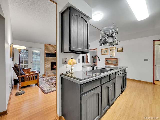 kitchen featuring a brick fireplace, light wood-style floors, a sink, and gray cabinetry