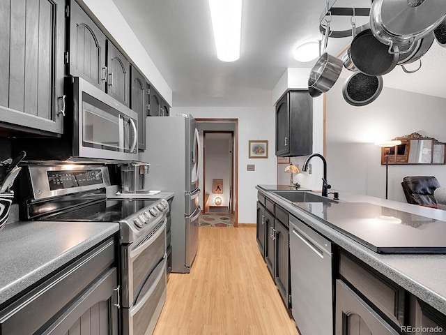 kitchen with light wood-type flooring, dark countertops, stainless steel appliances, and a sink