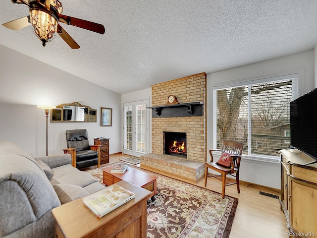 living room with a fireplace, light wood-style flooring, a textured ceiling, and ceiling fan