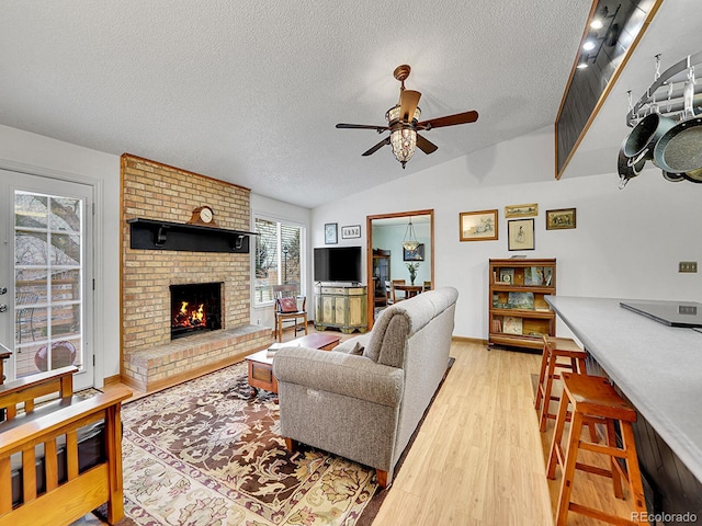 living area featuring a fireplace, light wood finished floors, lofted ceiling, ceiling fan, and a textured ceiling