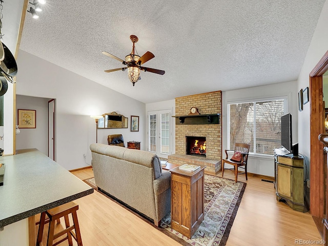 living room featuring vaulted ceiling, a fireplace, light wood-style flooring, and a ceiling fan