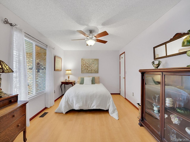 bedroom with light wood finished floors, visible vents, baseboards, ceiling fan, and a textured ceiling