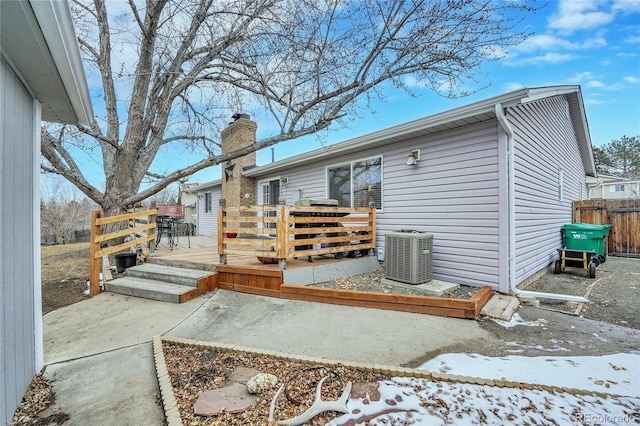 snow covered rear of property featuring central air condition unit, a chimney, fence, and a wooden deck