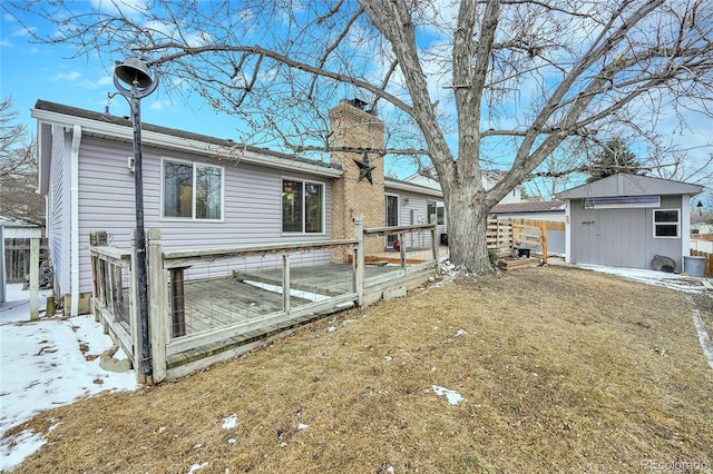 snow covered house featuring a chimney, a deck, a lawn, and an outdoor structure