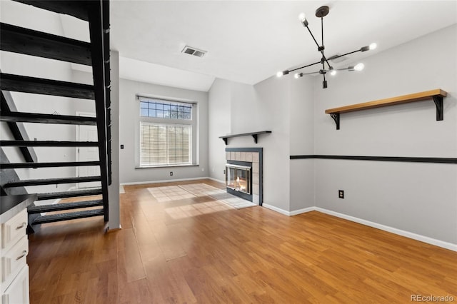 1885 S Quebec Way Unit A28, Denver, CO 80231 - unfurnished living room featuring light wood-style floors, a tile fireplace, baseboards, a chandelier, and stairs