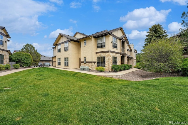 back of property featuring stone siding, a yard, stucco siding, and cooling unit