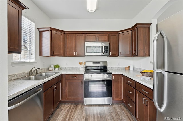 kitchen with appliances with stainless steel finishes, a sink, light countertops, and light wood finished floors