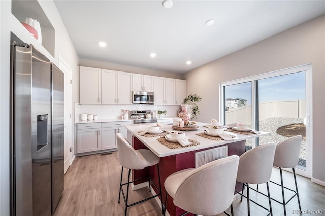 3879 N Shawnee St, Aurora, CO 80019 - kitchen with appliances with stainless steel finishes, a breakfast bar area, white cabinets, light wood finished floors, and recessed lighting