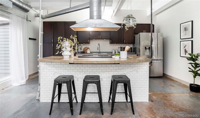 kitchen with island exhaust hood, baseboards, backsplash, concrete floors, and stainless steel refrigerator with ice dispenser