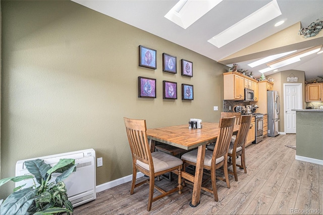 dining area featuring vaulted ceiling with skylight and light hardwood / wood-style flooring