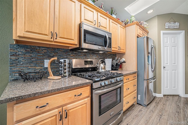 kitchen featuring light brown cabinetry, light wood-type flooring, backsplash, stainless steel appliances, and vaulted ceiling