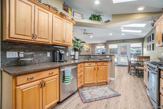 kitchen with ceiling fan, sink, stainless steel appliances, light hardwood / wood-style floors, and vaulted ceiling with skylight