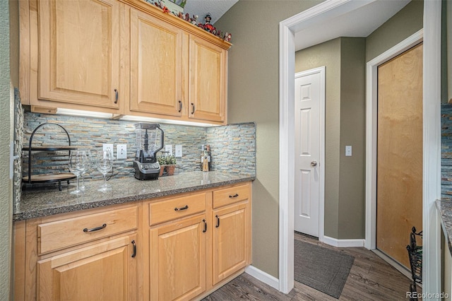 kitchen featuring decorative backsplash, light brown cabinetry, dark hardwood / wood-style floors, and dark stone counters