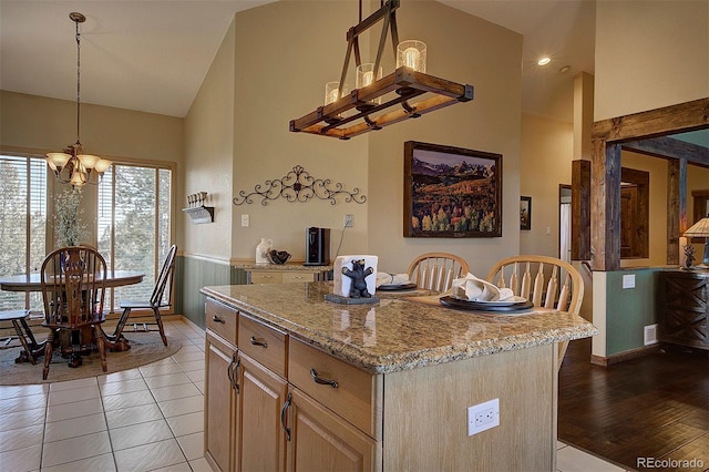 kitchen featuring light brown cabinetry, light stone counters, a center island, hanging light fixtures, and a notable chandelier