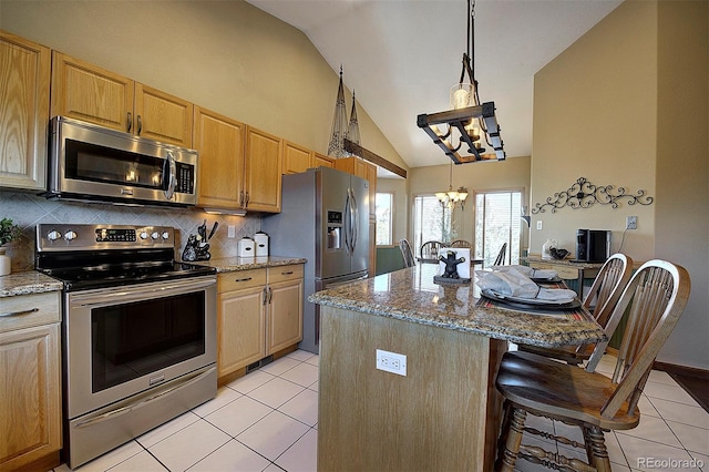 kitchen featuring a breakfast bar, stainless steel appliances, light stone countertops, a kitchen island, and decorative light fixtures