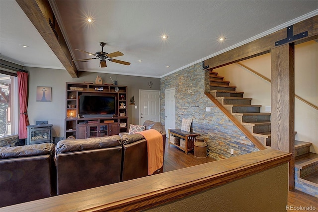 living room with hardwood / wood-style flooring, ceiling fan, beam ceiling, ornamental molding, and a wood stove