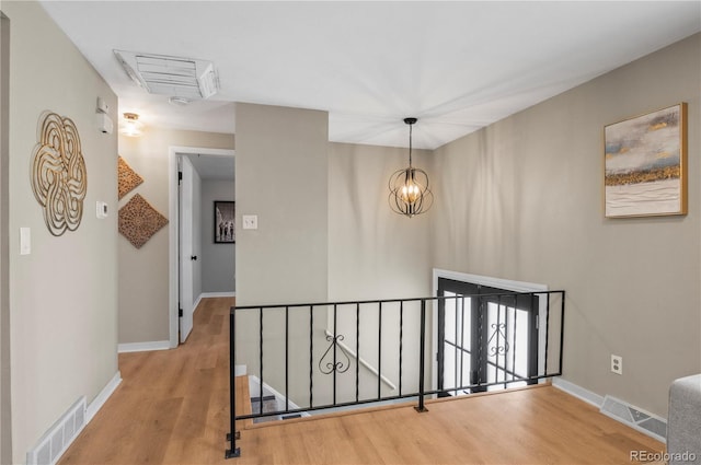 hall featuring a chandelier, an upstairs landing, wood finished floors, and visible vents