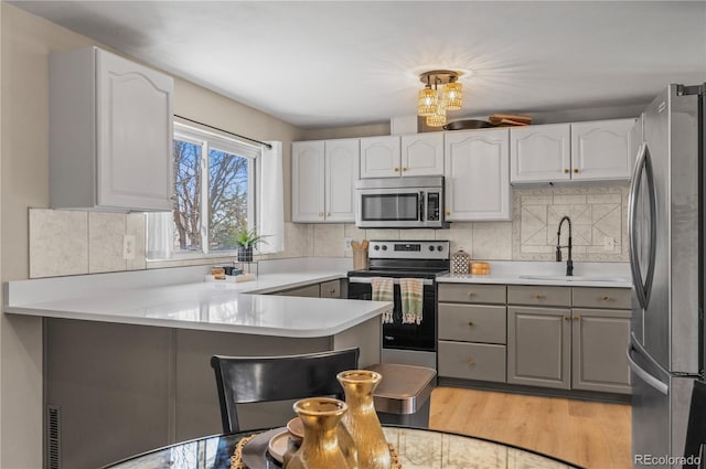 kitchen featuring a peninsula, light wood-style flooring, gray cabinetry, appliances with stainless steel finishes, and a sink