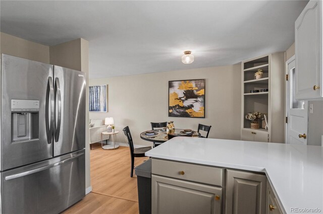 kitchen featuring stainless steel fridge with ice dispenser, light countertops, a peninsula, gray cabinetry, and light wood-style flooring